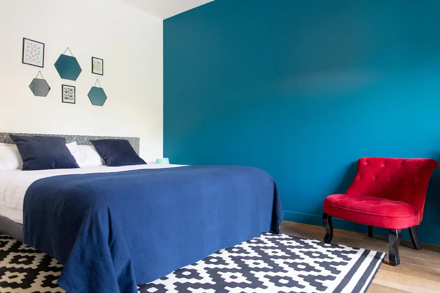 Heidelberg room: bed with a navy blue throw, red armchair and black and white rug