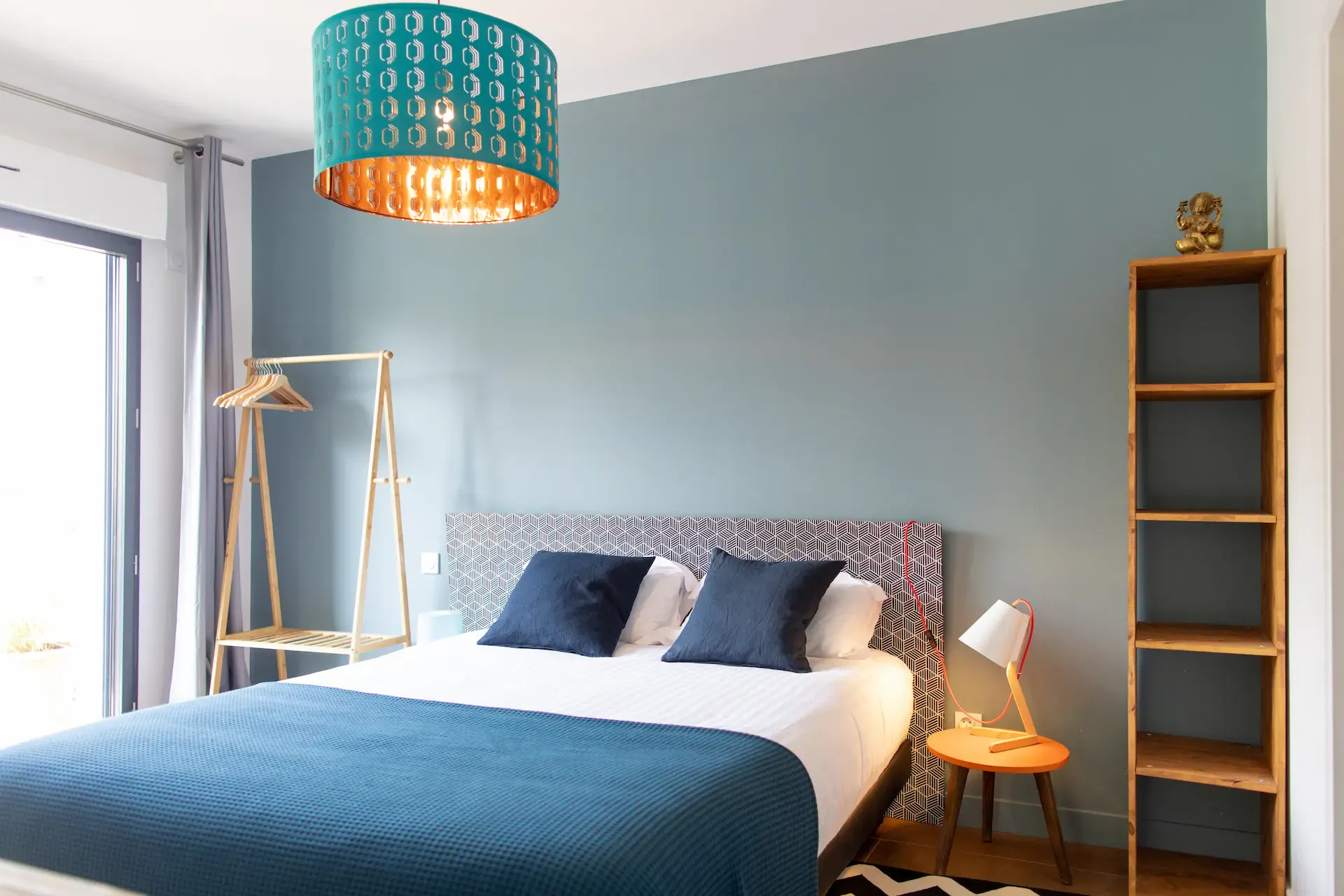 Chambre Hermosa : lit aux coussins bleus, suspension turquoise et étagère en bois