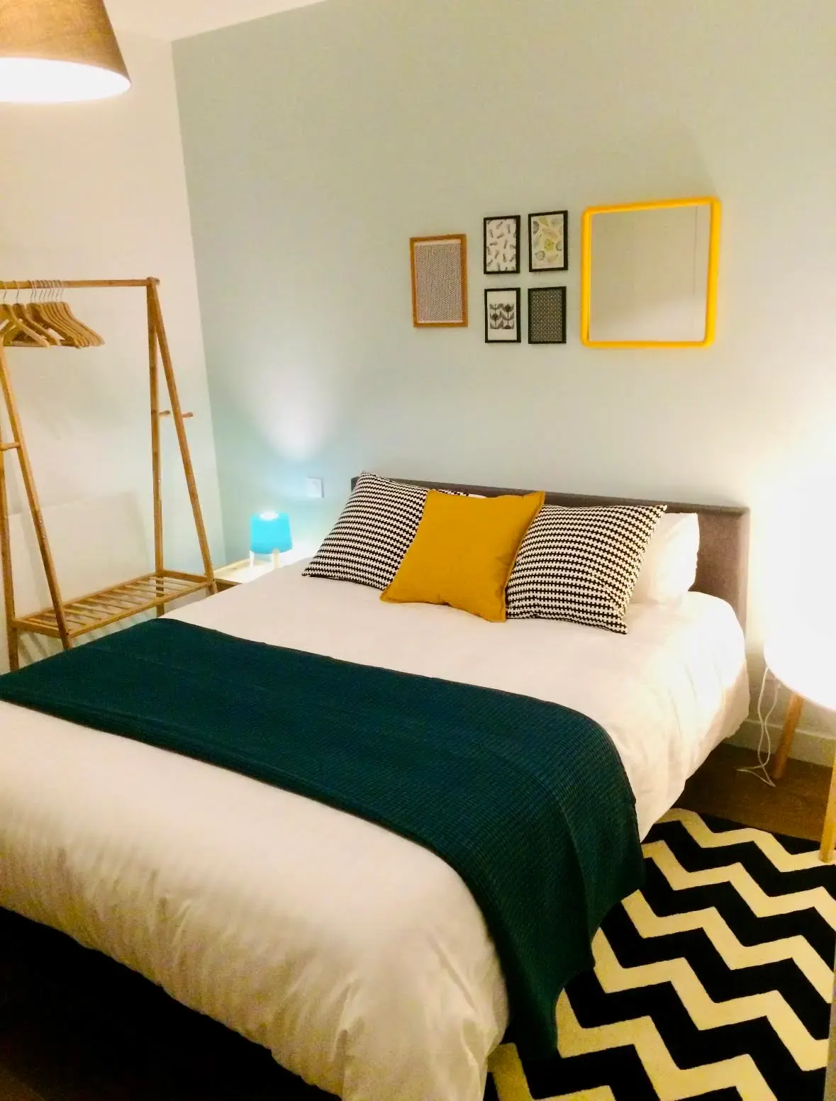 Palermo room: bed with striped and yellow cushions, green throw and chevron rug