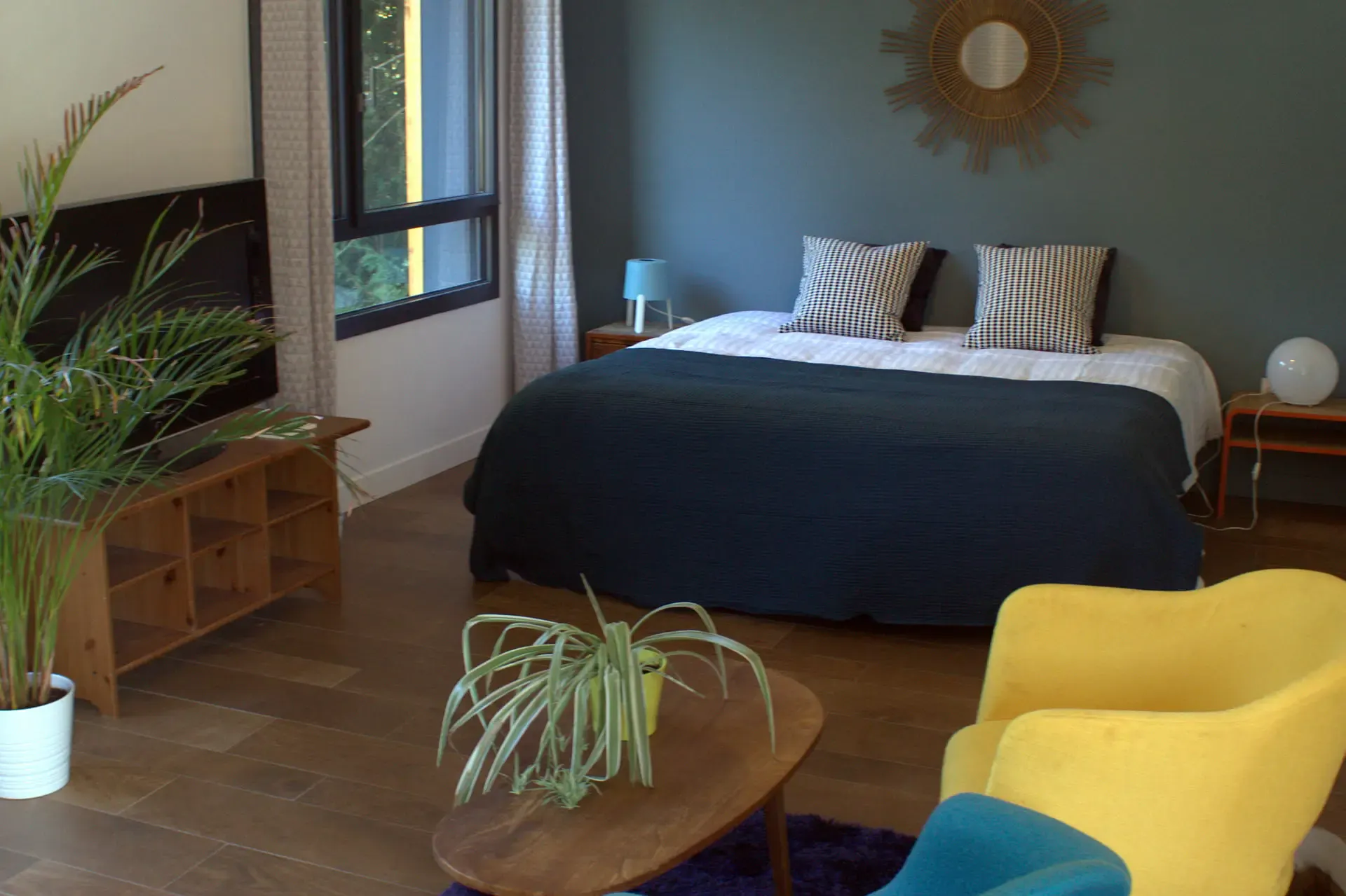 Chambre lumineuse au grand lit bleu marine, fauteuil jaune et plantes vertes