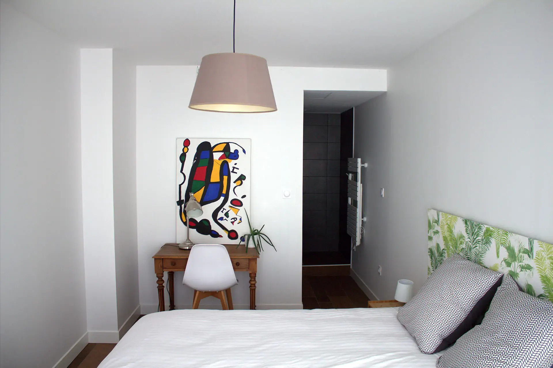 Chambre Gamboa : lit double au linge blanc, bureau en bois et tableau coloré au mur