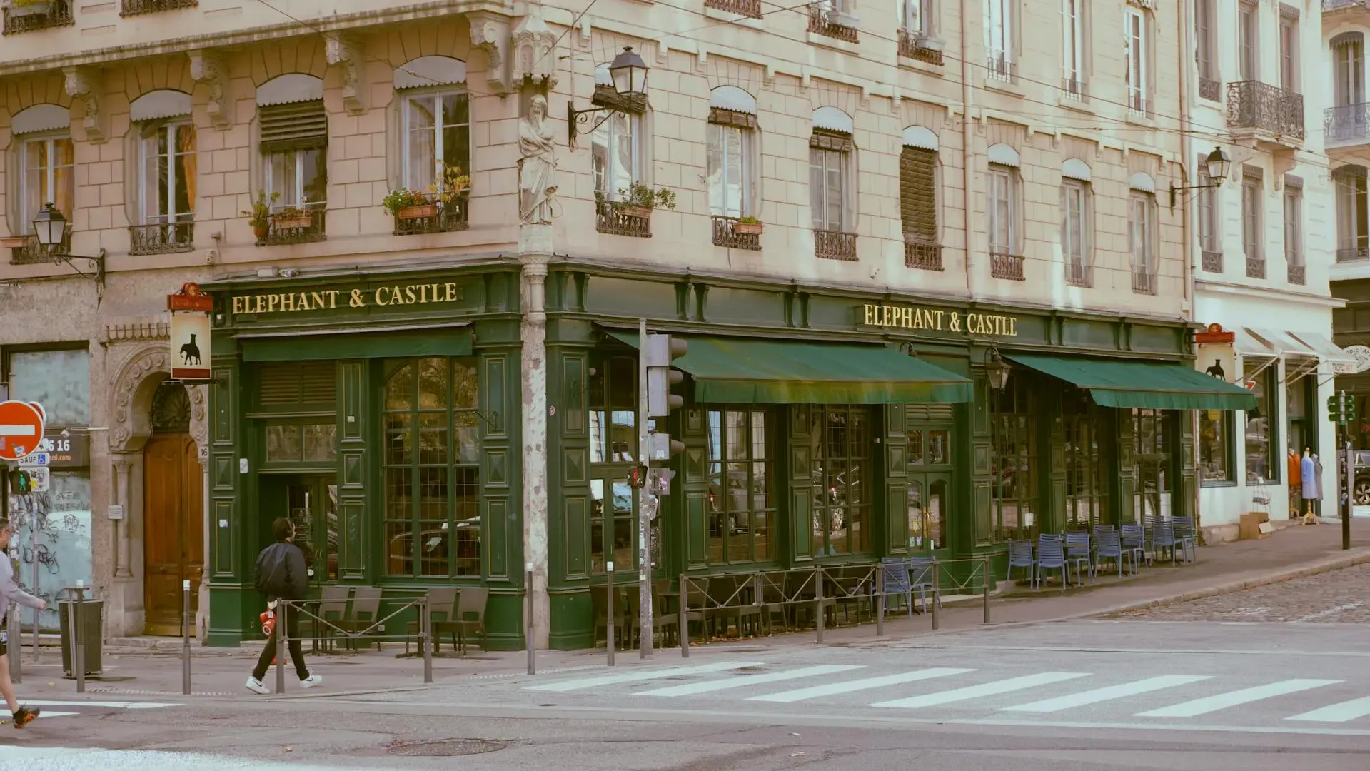 Façade d'un bouchon lyonnais aux devantures vertes et sa terrasse au pied d'un immeuble ancien