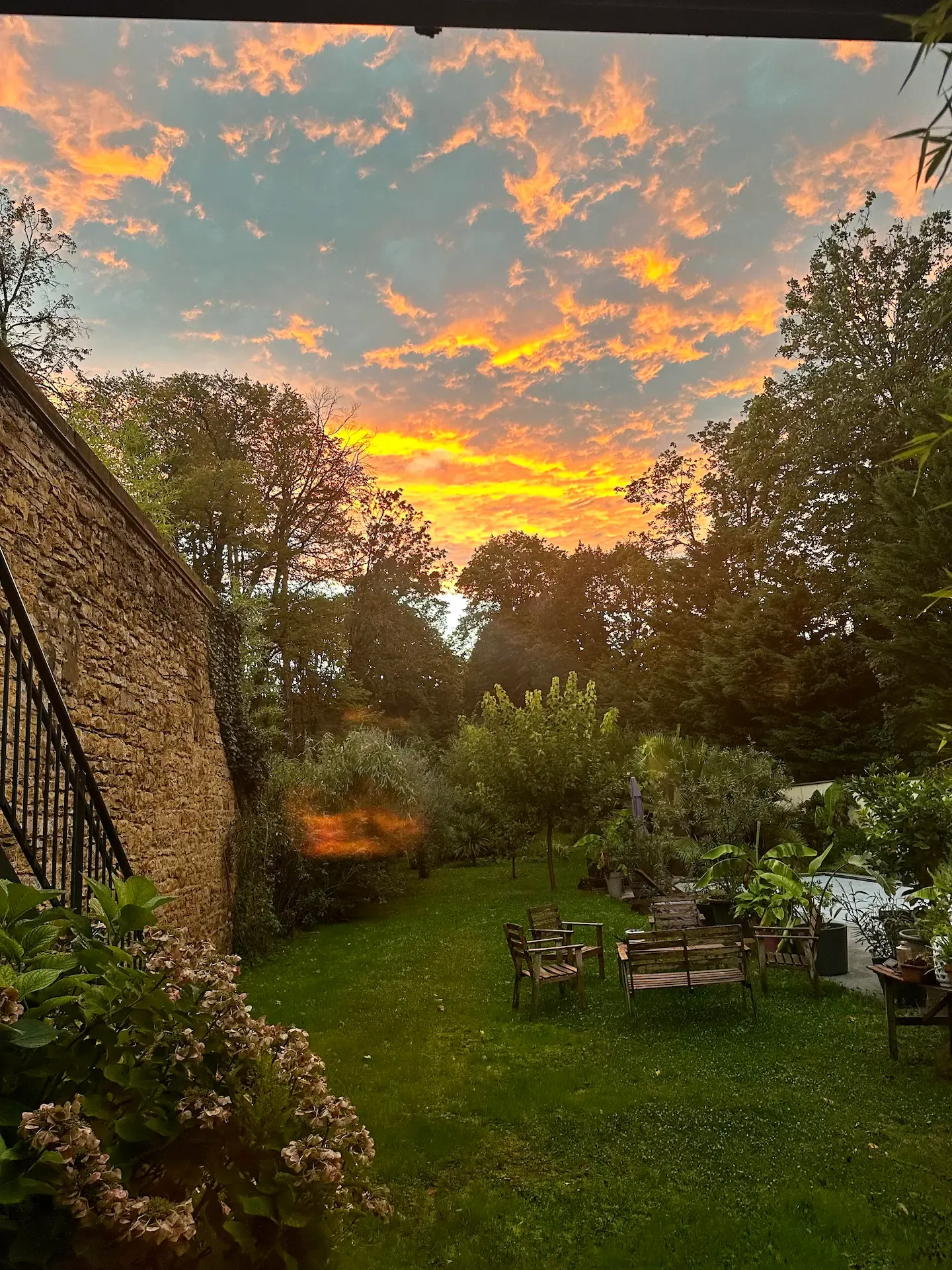 Jardin d'Effet Lodge au coucher du soleil, ciel orangé au-dessus des arbres et salon de jardin sur la pelouse