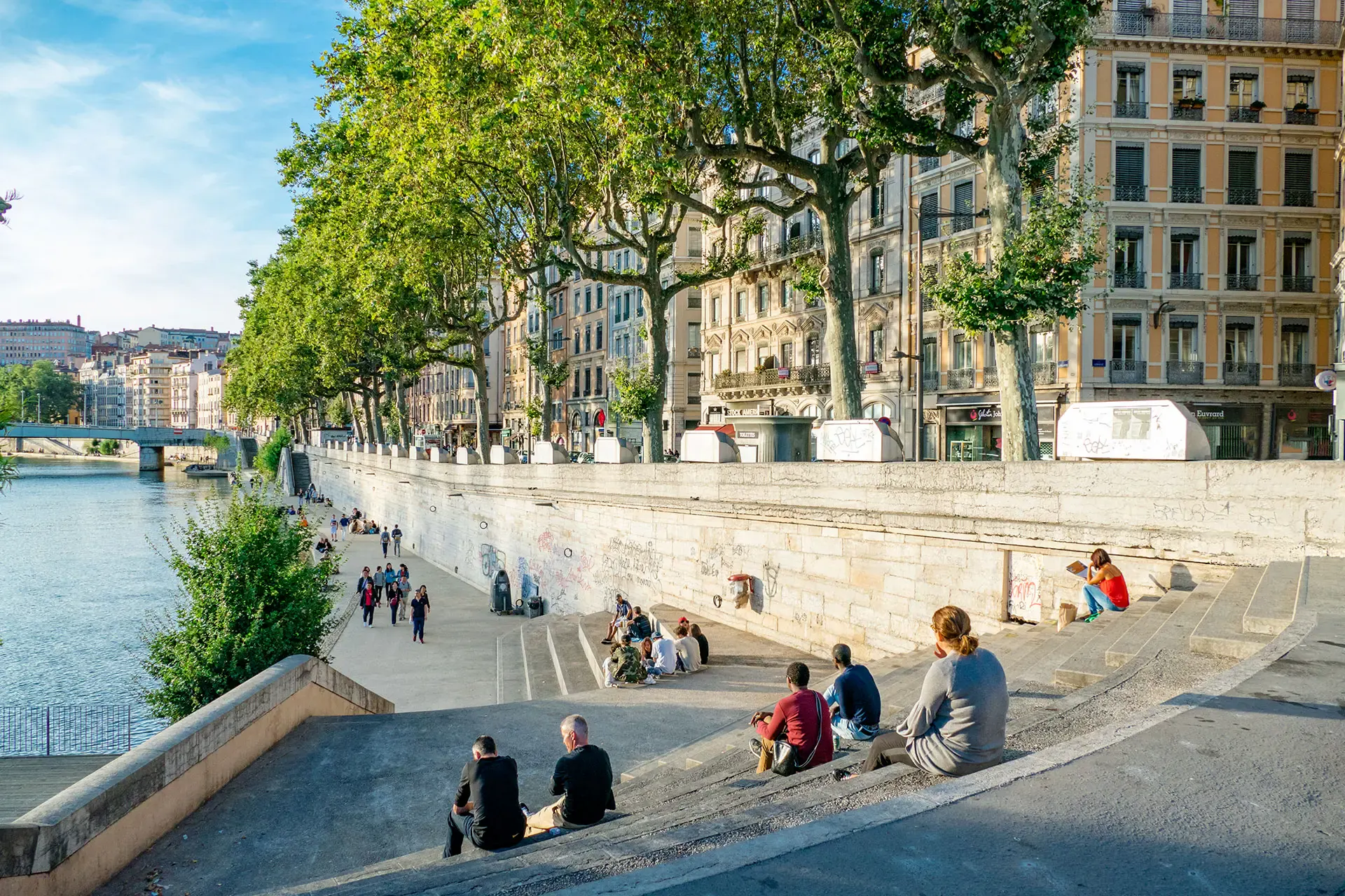 Walkers sitting on the steps of the Saône quays, under the plane trees