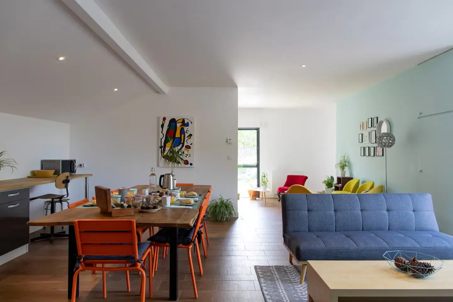 Salon et salle à manger communs : table en bois, chaises orange et canapé bleu